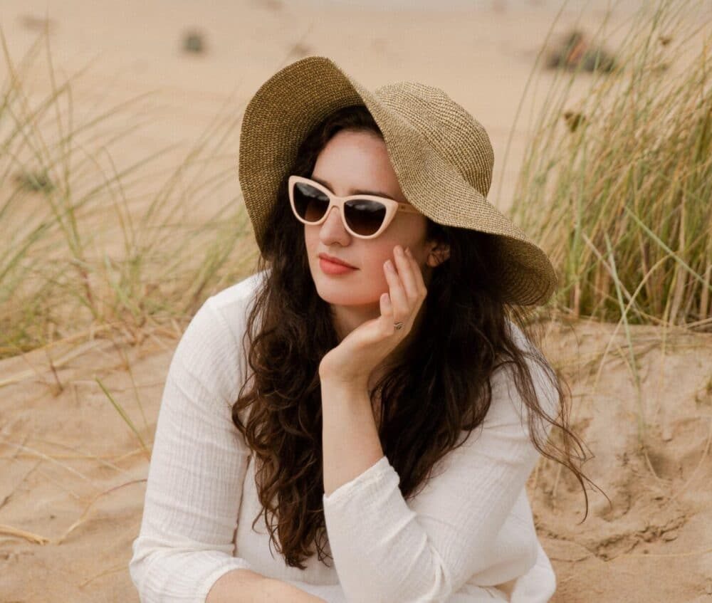Madeleine Olivia sitting on beach in sustainable Pala sunglasses