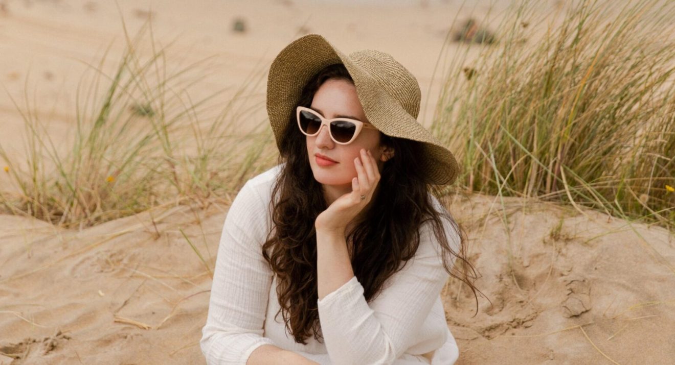 Madeleine Olivia sitting on beach in sustainable Pala sunglasses