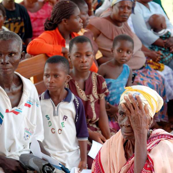 Older woman receiving eye test in rural village in Africa surrounded by children and adults waiting for thier own eye test.